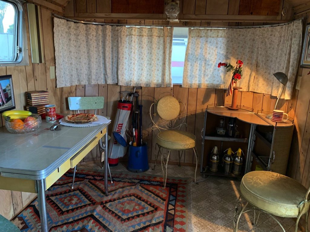 Airstream Spartan Manor, area living con tavolino, tendine, due sedie e portabottiglie in legno