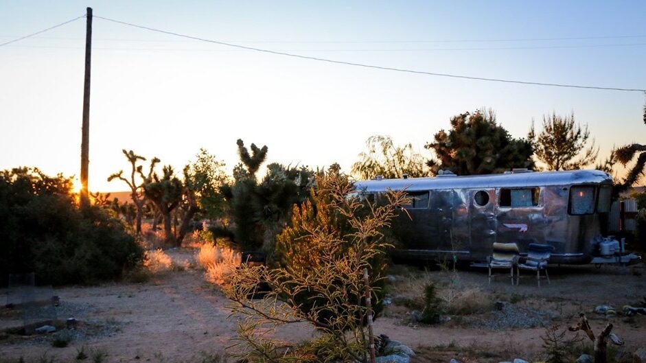 Vintage Spartan Trailer in una location desertica al tramonto, con cactus, sabbia e pochi alberi sparsi attorno