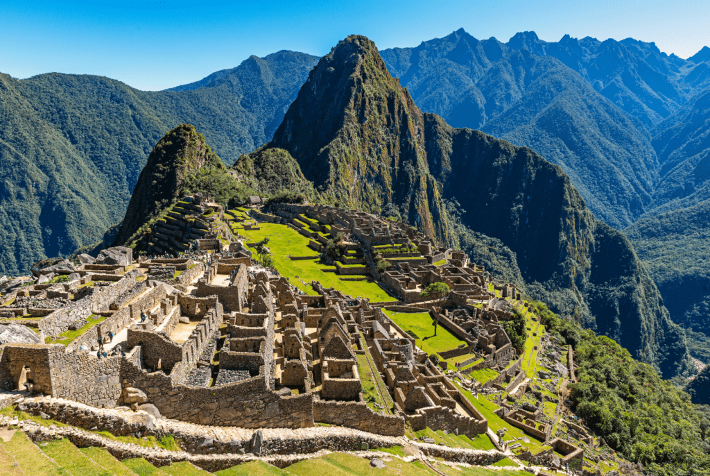 Veduta dall'alto delle rovine di Machu Picchu, con le caratteristiche montagne frastagliate sullo sfondo e un cielo terso e limpido sopra di loro 