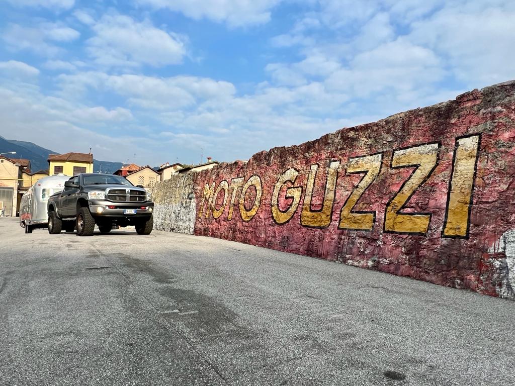 Muro con graffito con su scritto Moto Guzzi a caratteri cubitali e a lato un Airstream fiammante trainato da RAM