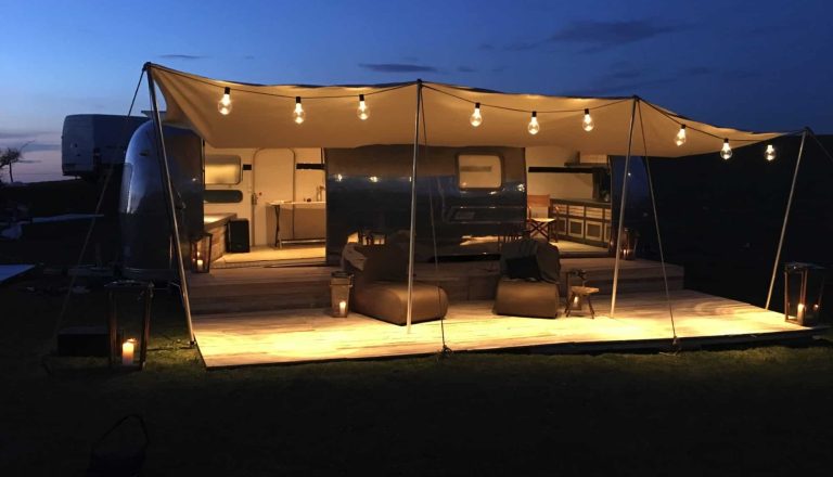 Airstream glamping in notturna, con decorazioni luminose ed un patio coperto da una tenda